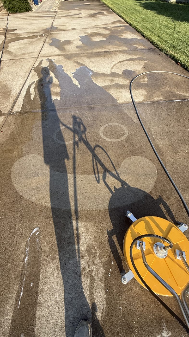 Rotary surface cleaner mid-pass on a dirty driveway, showing clean circles cut into the grime